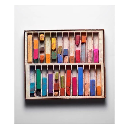 Overhead shot of a box filled with an array of colorful art pastels arranged neatly in rows against a white background.