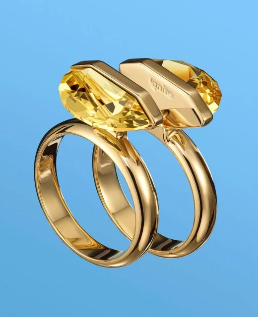 Close-up studio shot of two gold rings featuring yellow gems against a blue background, suitable for jewelry advertisement and accessory design.