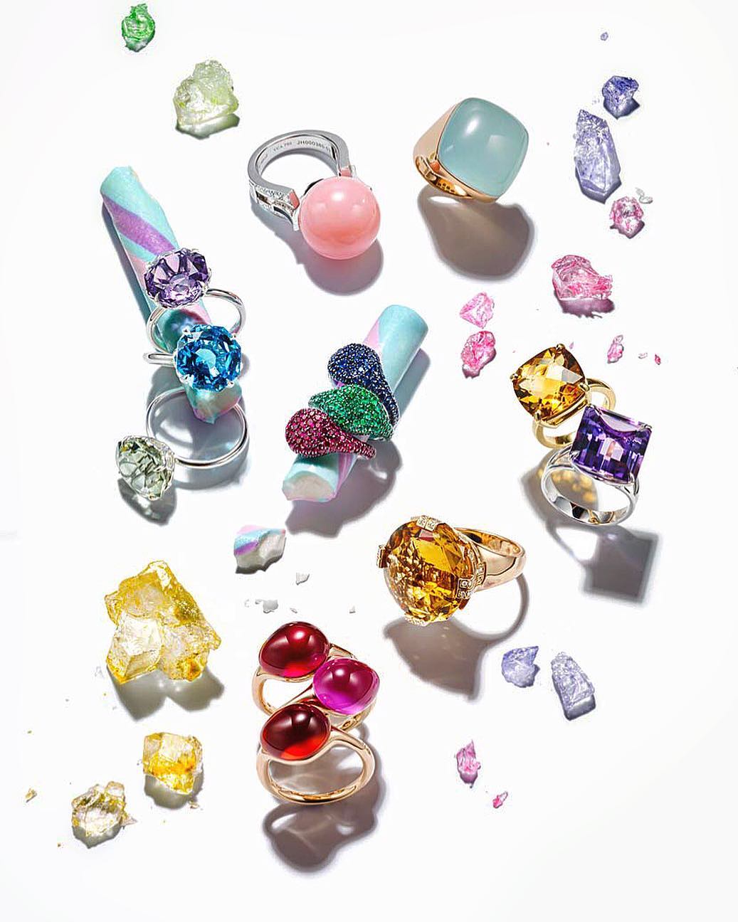 Arrangement of colorful gemstone rings and raw mineral stones on a white surface, jewelry photography showcasing various ring styles.