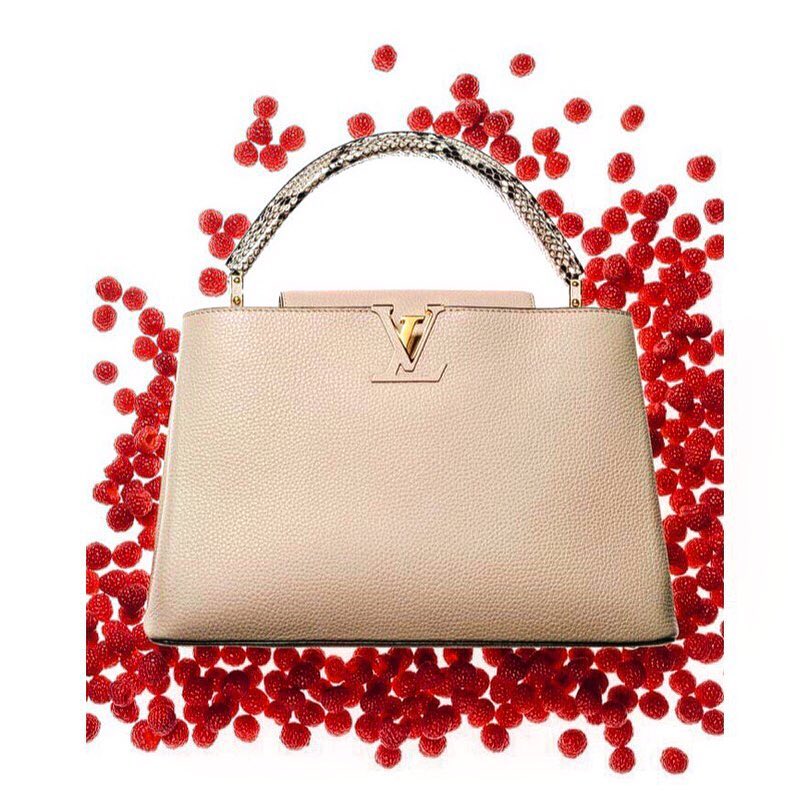 Designer handbag surrounded by scattered raspberries on a white background, creating a striking contrast and vibrant visual appeal.