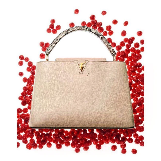 Designer handbag surrounded by scattered raspberries on a white background, creating a striking contrast and vibrant visual appeal.