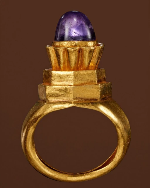 Gold ring with a purple cabochon gemstone, studio shot against a brown backdrop, jewellery design, close up view.