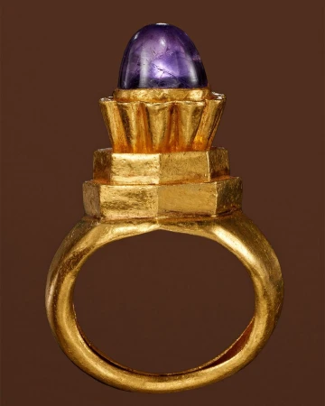 Gold ring with a purple cabochon gemstone, studio shot against a brown backdrop, jewellery design, close up view.