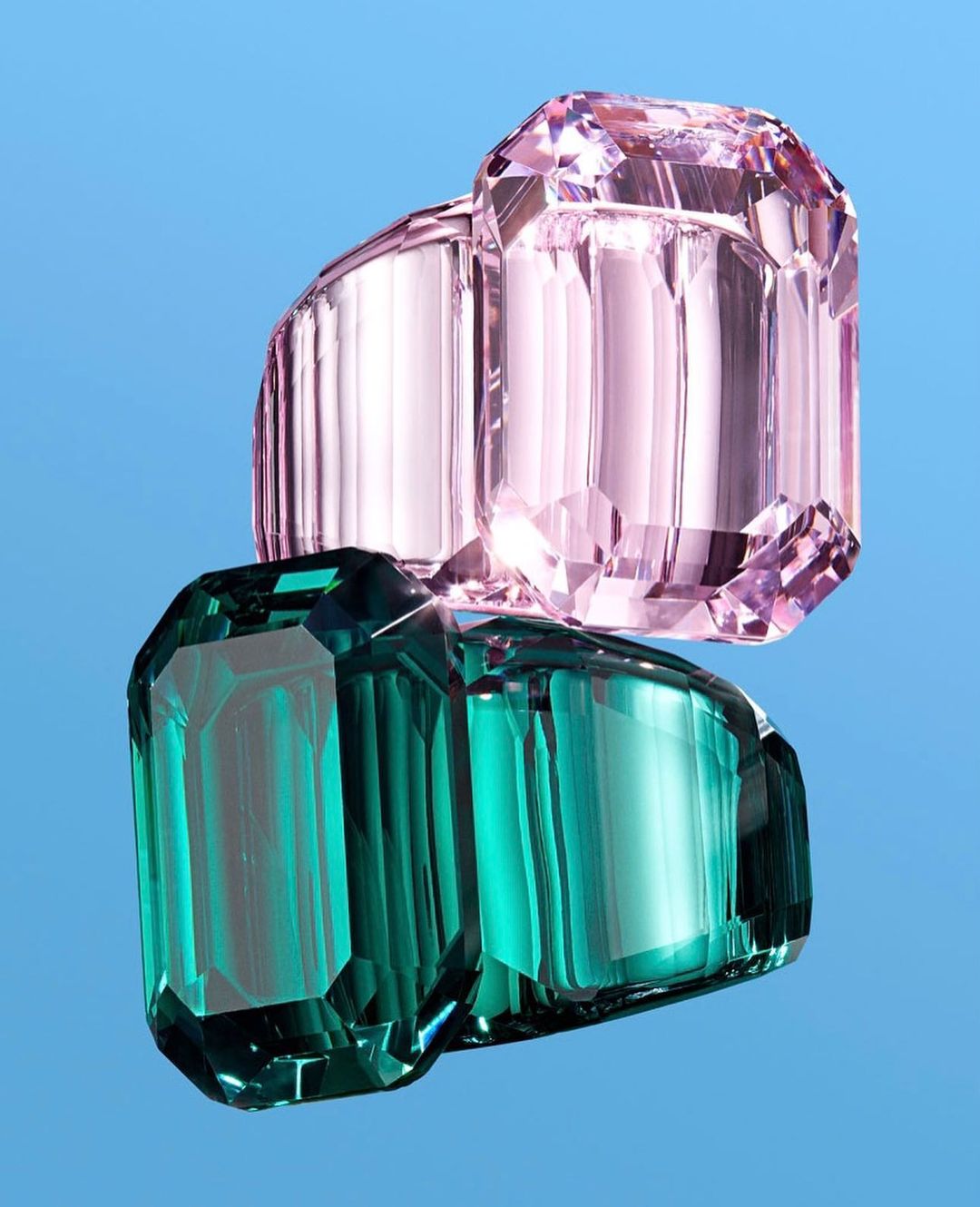 Close-up of stacked, faceted emerald-cut rings in pink and green against a solid blue background, reflecting light.