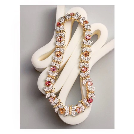 Elegant gold necklace featuring butterfly and flower motifs adorned with sparkling white and pink gemstones, displayed on a soft gray backdrop.
