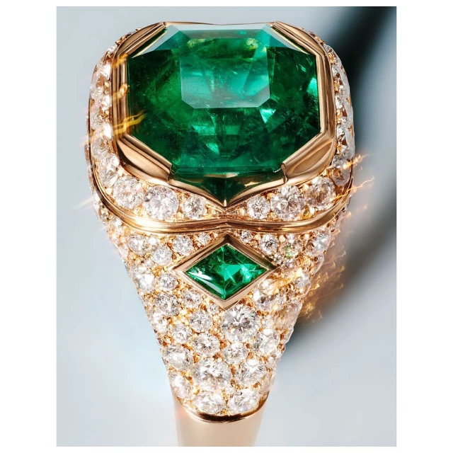 Macro photograph of a gold ring with an emerald-cut green emerald surrounded by small diamonds against a light blue background.