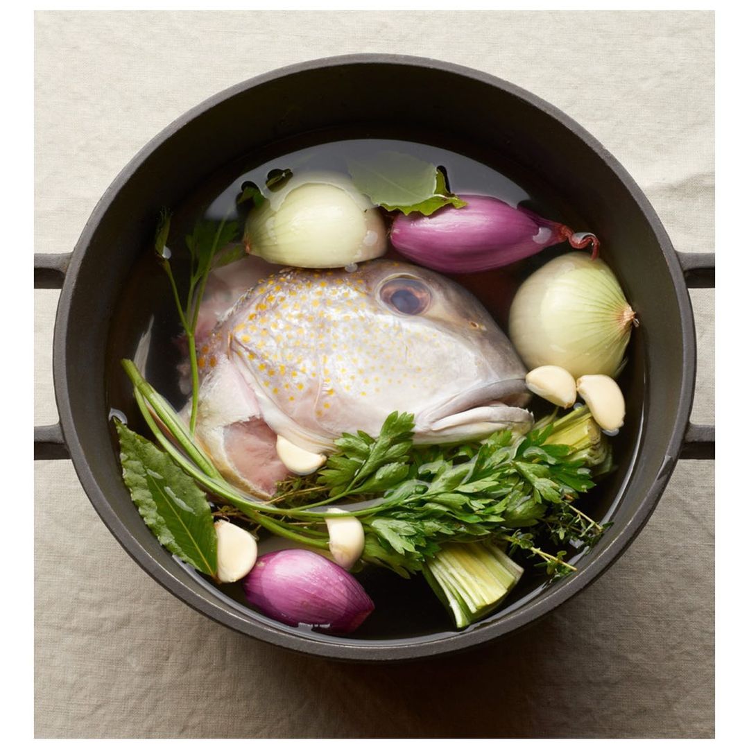 Overhead shot of fish head soup in a cast iron pot with onions, garlic, herbs, and broth.