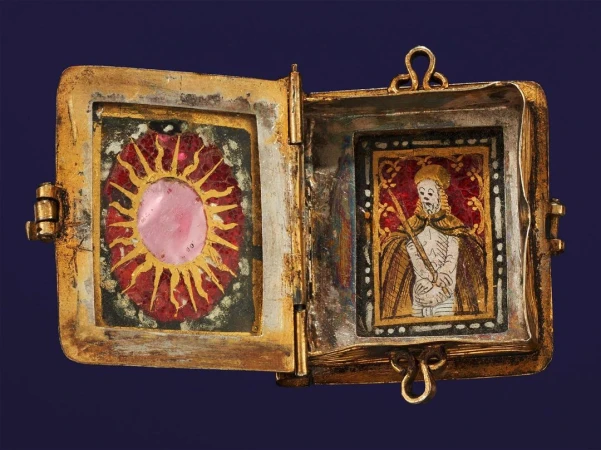 Open golden locket showcasing religious art, one side featuring a pink sun-like image, the other an illustrated religious figure.