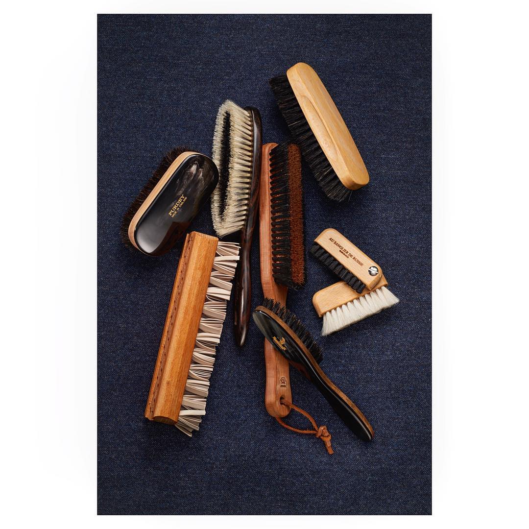 Arrangement of wooden-handled brushes with black or white bristles on a textured dark blue textile background, showcasing bristles and handles.
