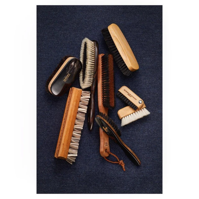 Arrangement of wooden-handled brushes with black or white bristles on a textured dark blue textile background, showcasing bristles and handles.