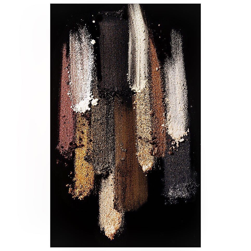 Close-up of brown, gold, black, and white eyeshadow swatches on a dark surface, showcasing cosmetic color palettes and makeup textures.