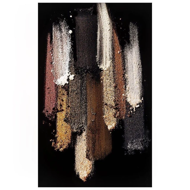 Close-up of brown, gold, black, and white eyeshadow swatches on a dark surface, showcasing cosmetic color palettes and makeup textures.