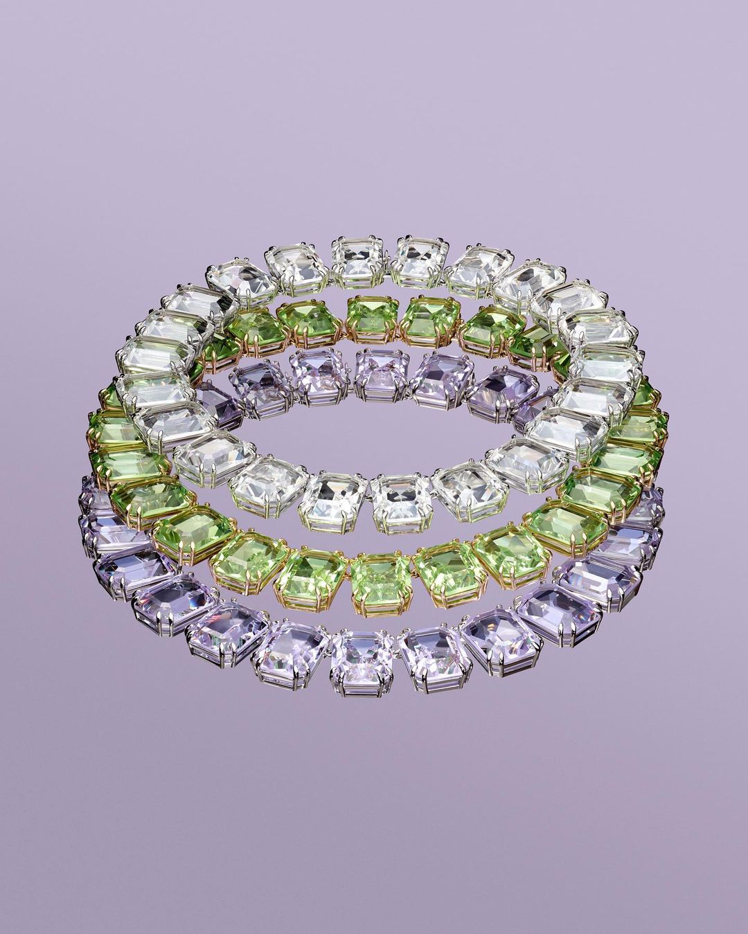 Three circular necklaces featuring clear, green, and purple square-cut gemstones, displayed on a reflective lavender surface in a studio setting.