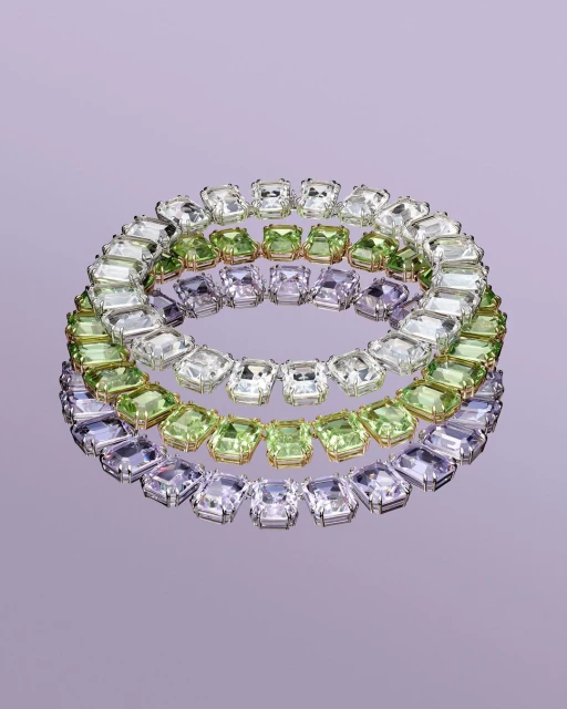 Three circular necklaces featuring clear, green, and purple square-cut gemstones, displayed on a reflective lavender surface in a studio setting.