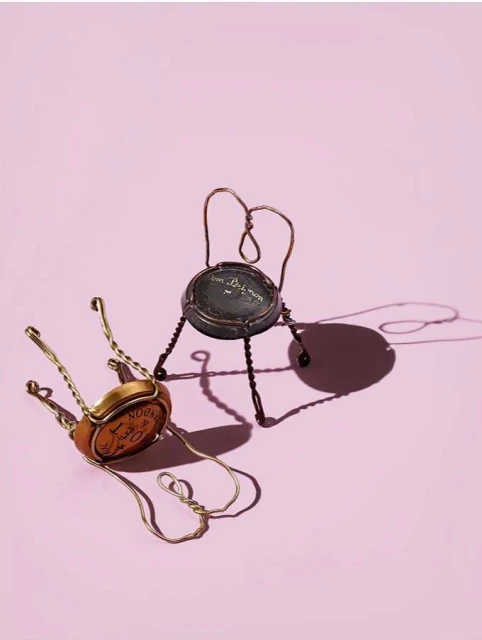Artistic shot of two miniature chairs crafted from champagne corks and wire, creating a whimsical still life on a pink backdrop.