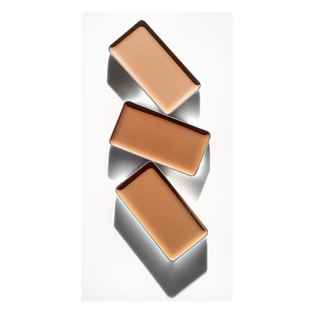 Three shades of face powder arranged in a vertical stack on a light surface, each with a dark border and shadow, shot with studio lighting.