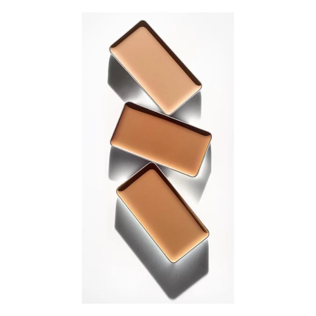Three shades of face powder arranged in a vertical stack on a light surface, each with a dark border and shadow, shot with studio lighting.