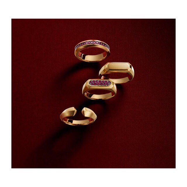 Still life of four gold rings with and without embedded rubies, arranged on a textured dark red surface, studio lighting.