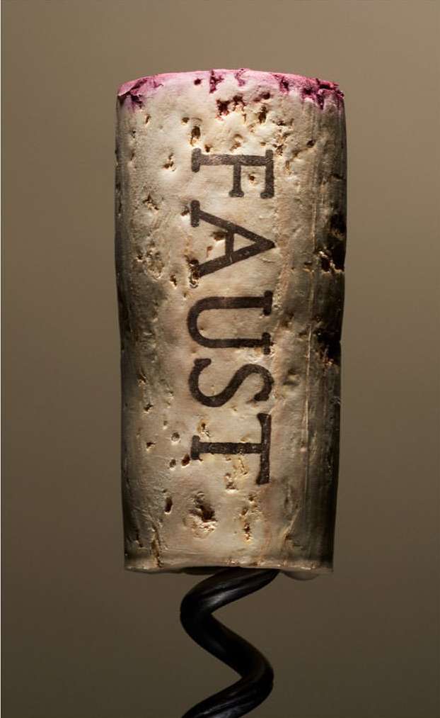 Macro photograph of a wine cork with the word 'FAUST' engraved, displaying its texture, with a wine opener corkscrew at the bottom.