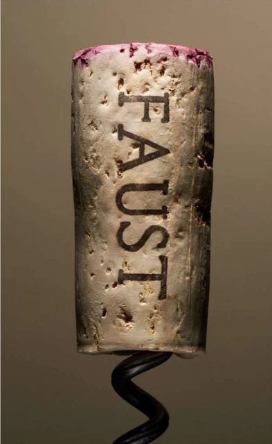Macro photograph of a wine cork with the word 'FAUST' engraved, displaying its texture, with a wine opener corkscrew at the bottom.