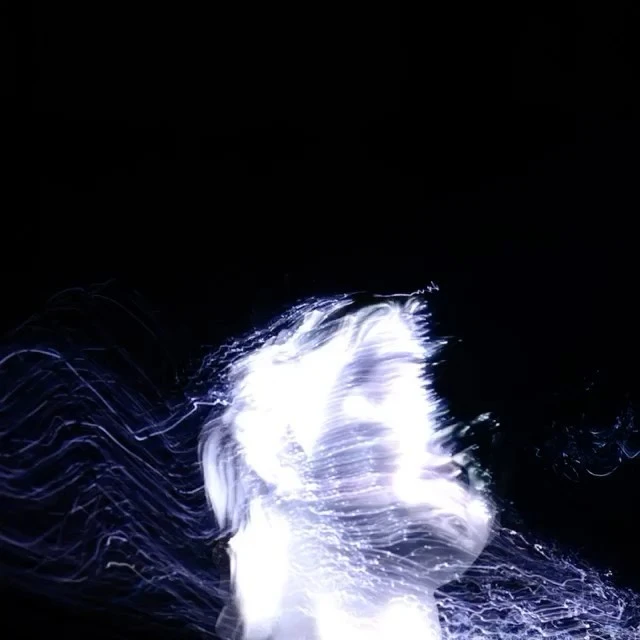 Abstract portrait of a person with long exposure and light painting, creating a glowing and ethereal aesthetic against a black backdrop.