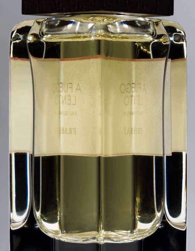 Close-up of a clear glass perfume bottle with a dark brown cap, filled with light yellow liquid, and featuring Spanish text on the label.