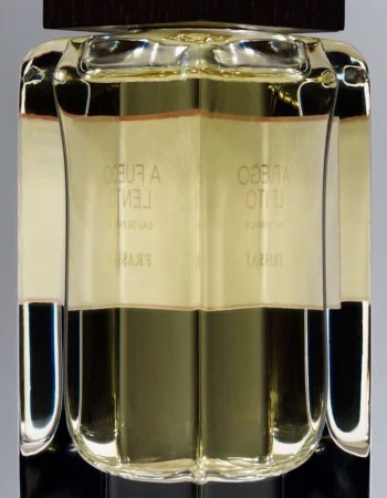 Close-up of a clear glass perfume bottle with a dark brown cap, filled with light yellow liquid, and featuring Spanish text on the label.
