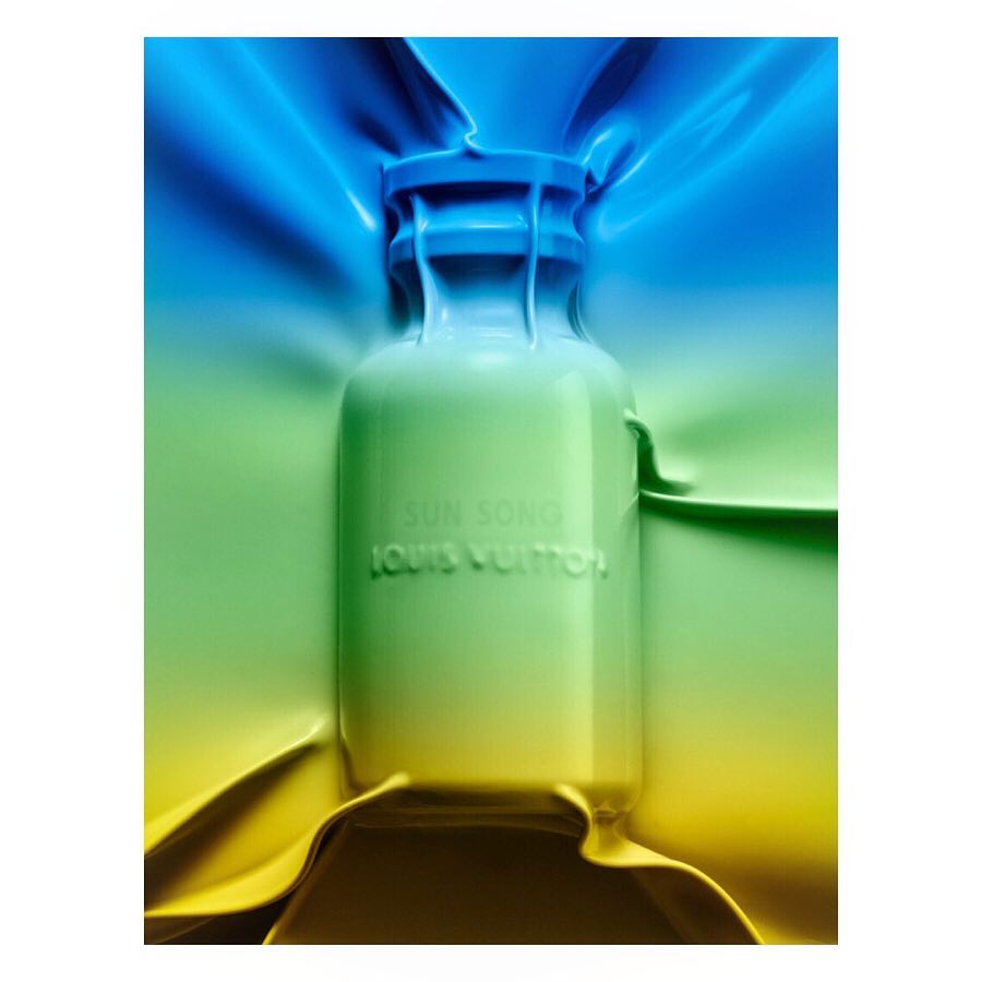 Close-up studio shot of a Louis Vuitton perfume bottle transitioning from blue to green to yellow, encased in draping plastic.
