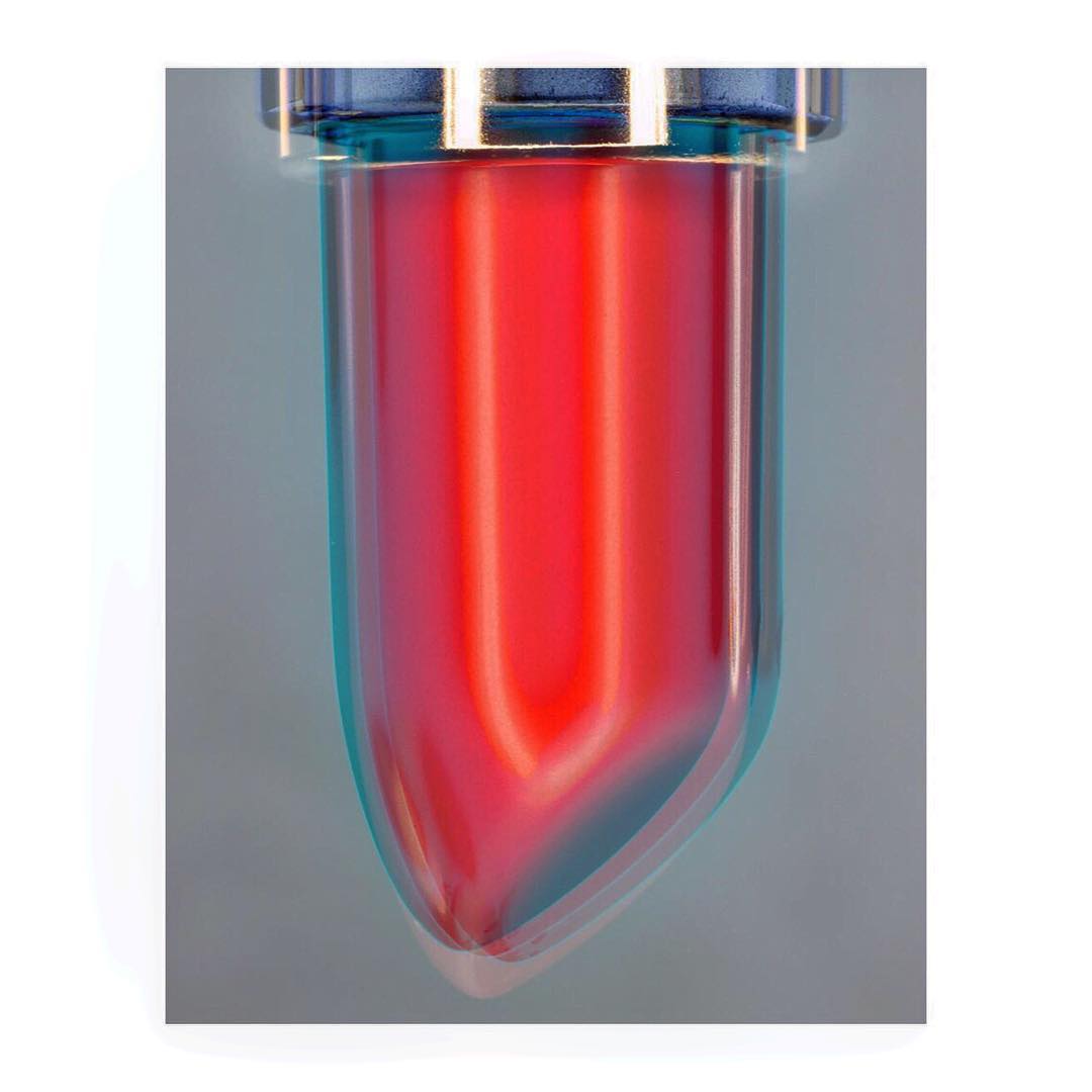 Close-up of a blue-topped, transparent container filled with a vibrant, luminous red liquid, showcasing its texture and color gradient.