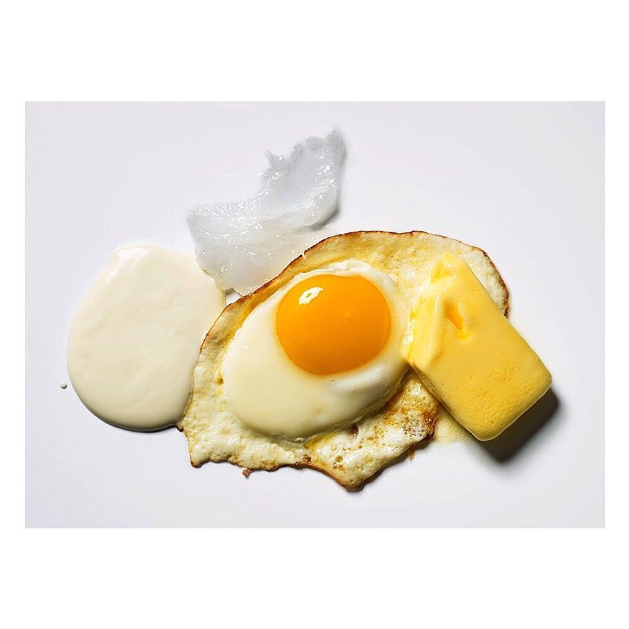 Close-up studio shot of a fried egg with runny yolk, topped with a pat of melting butter and a dollop of white creamy sauce.