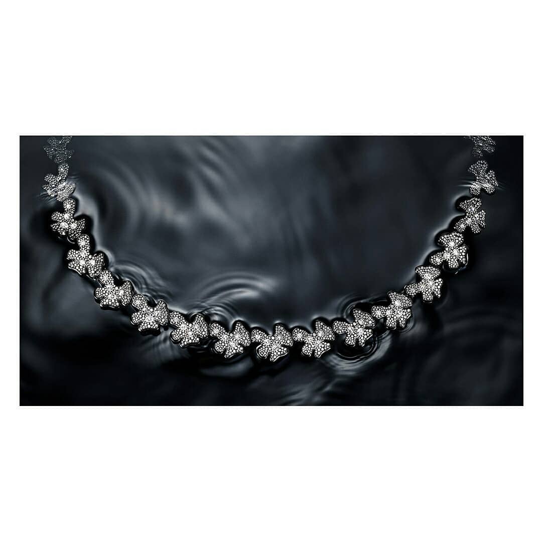 Elegant diamond necklace featuring floral designs on a dark rippled water surface creating a sophisticated jewelry product shot.