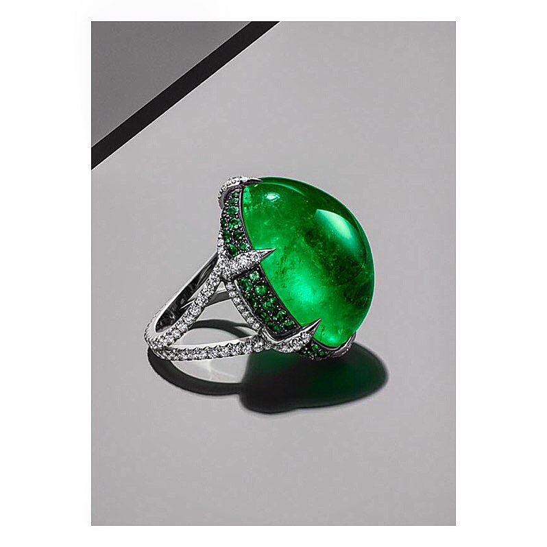 Close-up of a ring featuring a large, green cabochon gemstone surrounded by smaller stones, highlighting jewelry design and craftsmanship.
