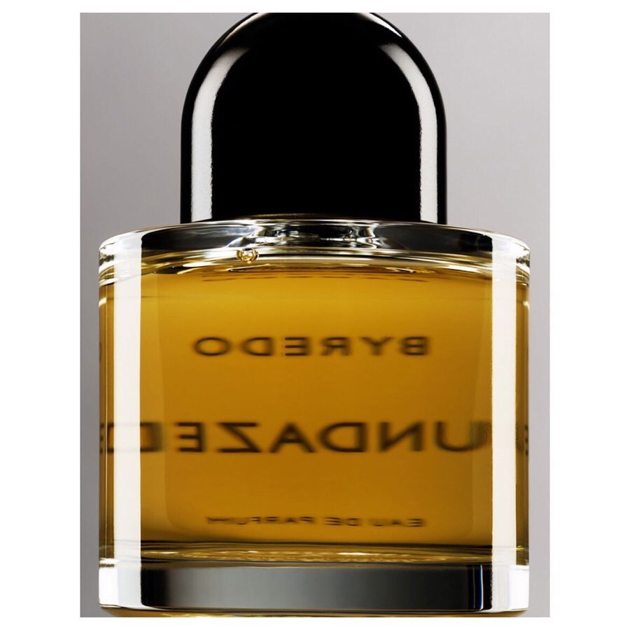 Byredo Sundazed fragrance in a square clear-glass bottle with a black dome-shaped cap against a neutral gray background in studio lighting.