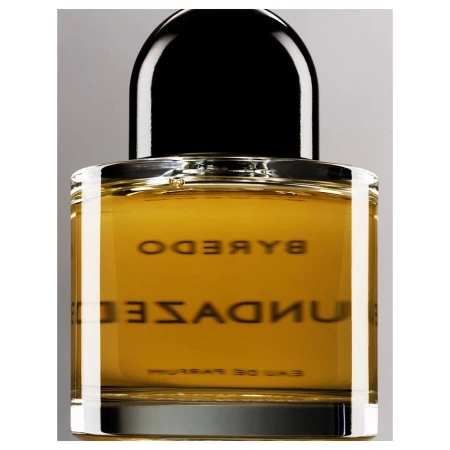 Byredo Sundazed fragrance in a square clear-glass bottle with a black dome-shaped cap against a neutral gray background in studio lighting.