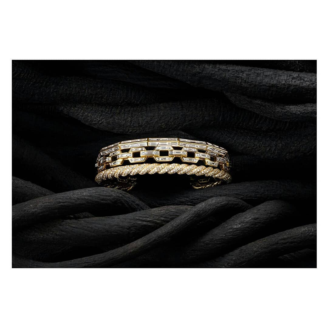 Close-up of a gold chain link bracelet and gold twisted bracelet displayed on black fabric. Jewellery and fashion photography.