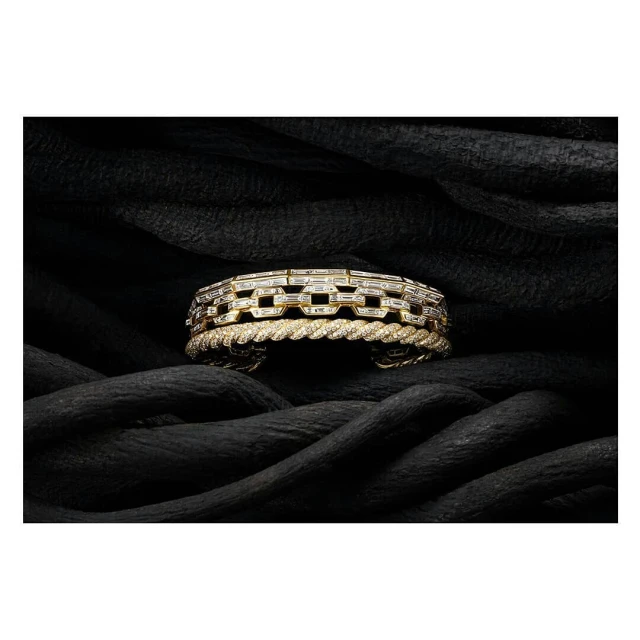 Close-up of a gold chain link bracelet and gold twisted bracelet displayed on black fabric. Jewellery and fashion photography.