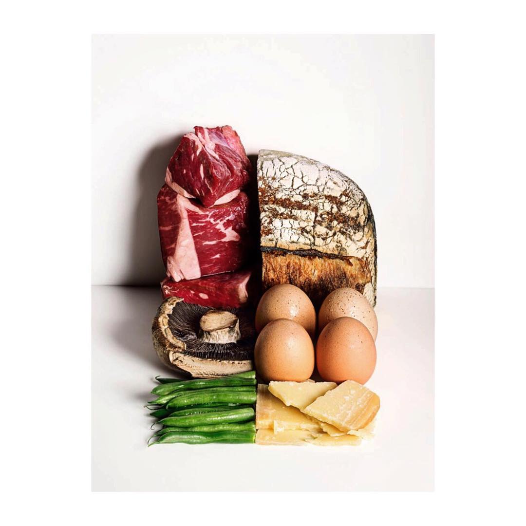 Studio shot of fresh food ingredients: raw beef steaks, sourdough bread, eggs, mushroom, green beans, and parmesan cheese on white.