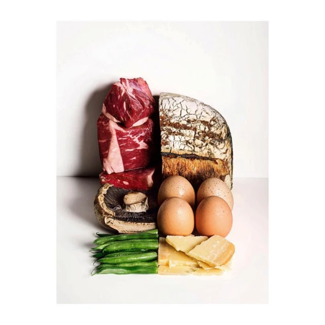 Studio shot of fresh food ingredients: raw beef steaks, sourdough bread, eggs, mushroom, green beans, and parmesan cheese on white.