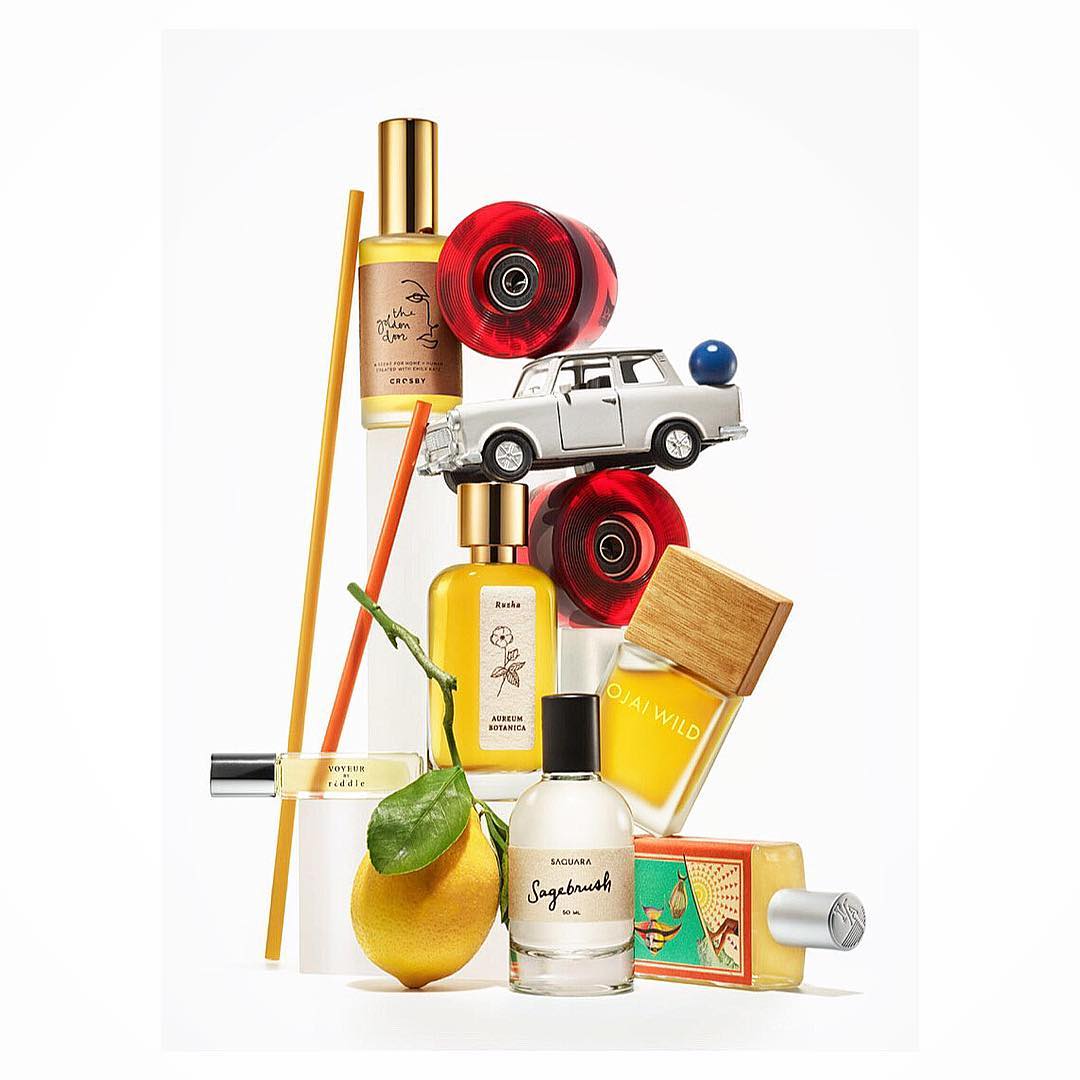 Still life featuring perfume bottles, a lemon, toy car, and skate wheels arranged on a white background with soft, diffused lighting.