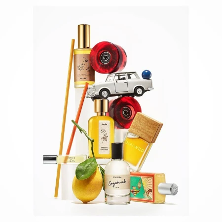 Still life featuring perfume bottles, a lemon, toy car, and skate wheels arranged on a white background with soft, diffused lighting.