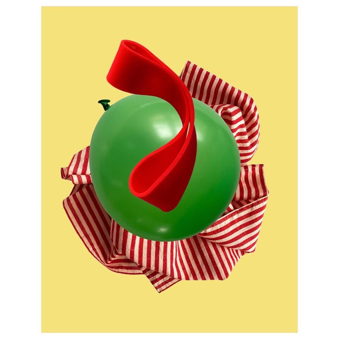 Still life of a green balloon with red ribbon and striped cloth against a yellow background, perfect for celebration or party decor.