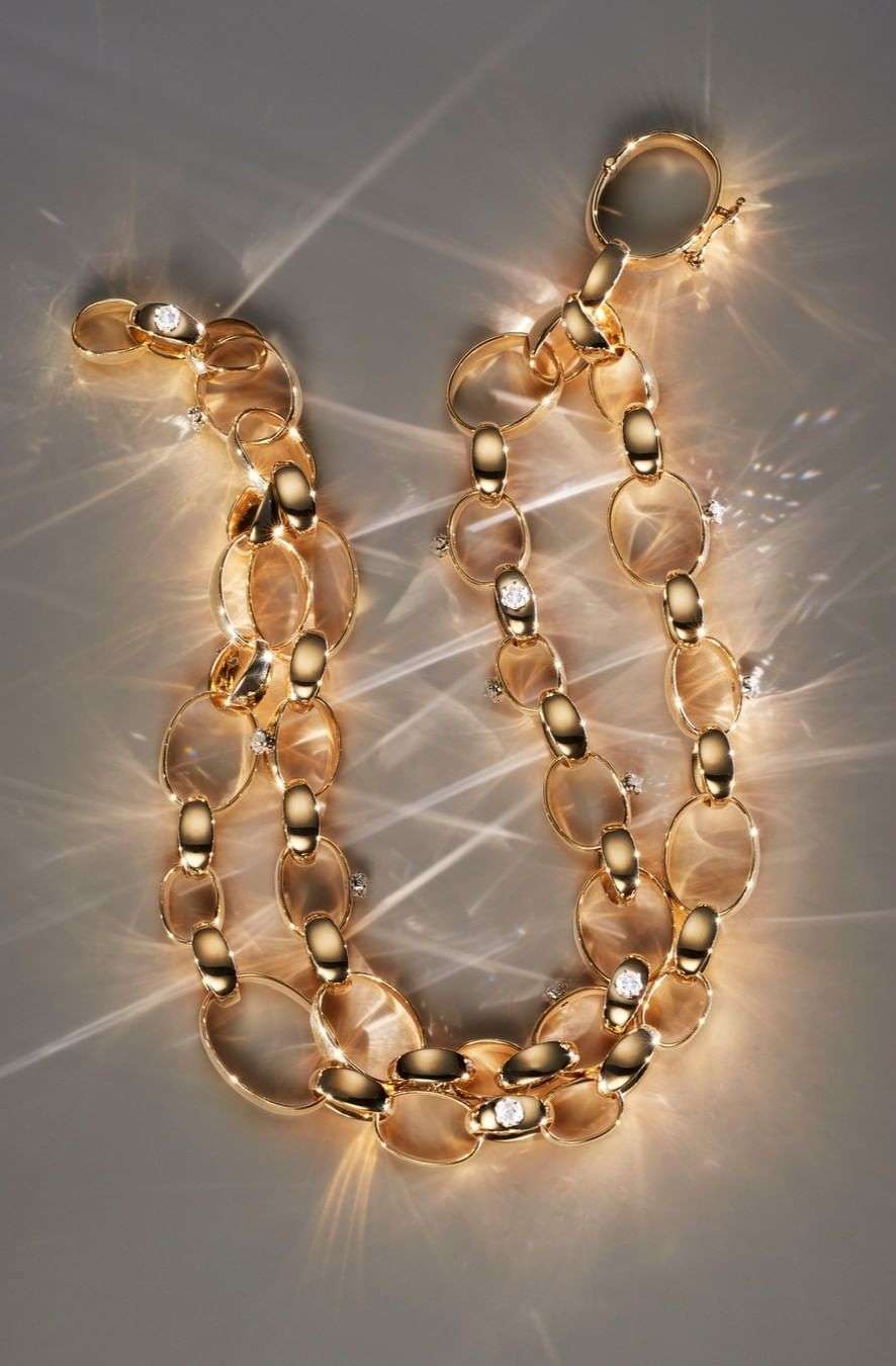 Elegant golden chain necklace jewelry with sparkling diamond accents, displayed against a neutral backdrop with dramatic light reflections.