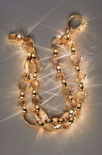 Elegant golden chain necklace jewelry with sparkling diamond accents, displayed against a neutral backdrop with dramatic light reflections.