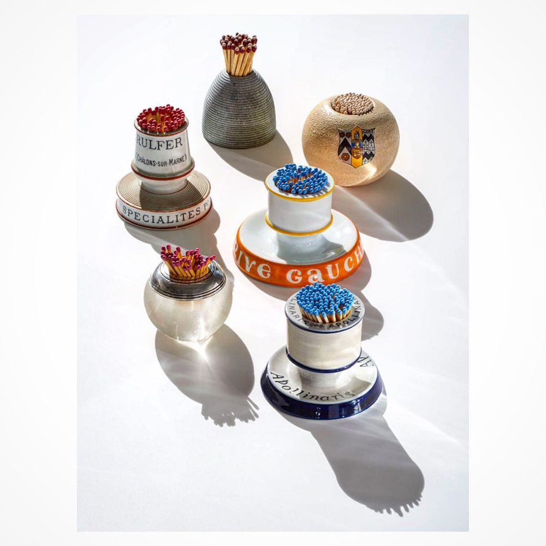 Still life composition featuring a collection of decorative match holders with matches, set against a stark white background and hard shadows.