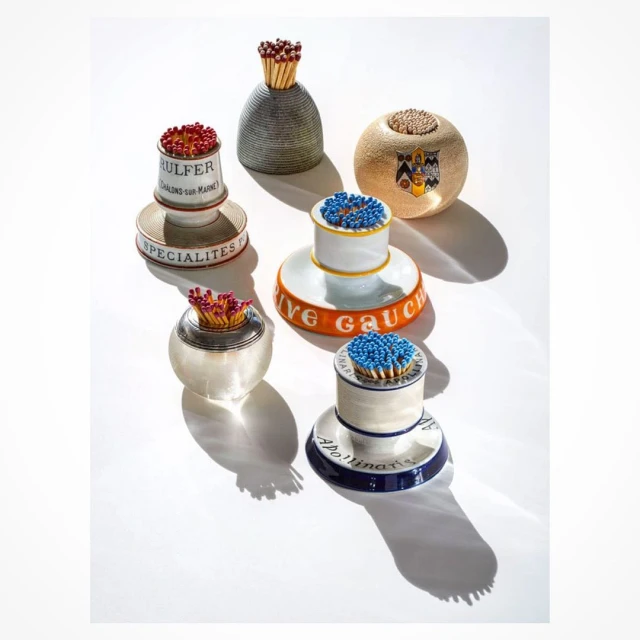 Still life composition featuring a collection of decorative match holders with matches, set against a stark white background and hard shadows.