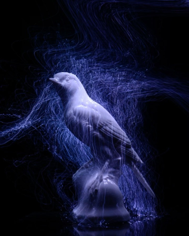 Illuminated ceramic bird figurine on a reflective surface against a dark backdrop with blue light trails around the bird.