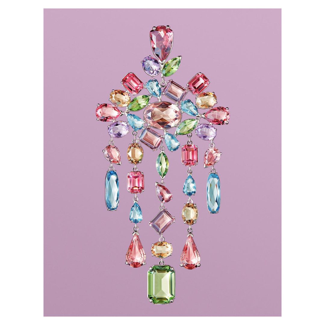 Elegant arrangement of multi-colored gemstones in a chandelier-like cascading design on a light purple background. Jewellery advertisement.