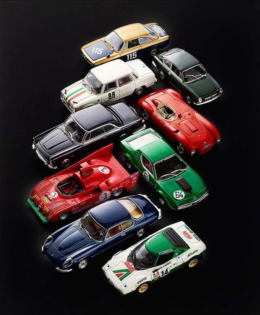 Collection of vintage car model toys displayed on black background, showcasing multiple colors and designs.