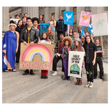 Group of youth activists stand on building steps holding signs with messages of protest and environmental awareness for a demonstration.