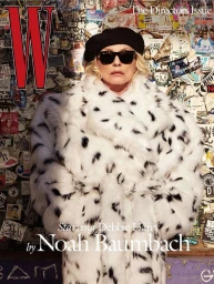 Debbie Harry wearing a white faux fur coat, black beret, and sunglasses against a sticker-covered wall for W Magazine.